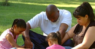 Family holding hands outside, bowing heads in prayer