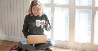 Smiling woman holding a cup of coffee while working on a laptop