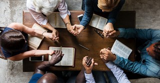 People praying around a table, the first will be last no one who has left home or brothers or sisters or mother or father or children or fields for me