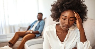 Close-up of an unhappy woman with her husband ignoring her in the background