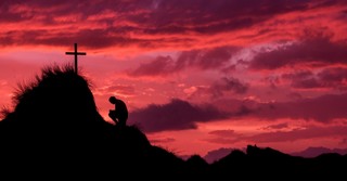 Man kneeling in front of the cross on a hill