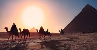 Silhouette of people riding camels at sunset by the pyramids in Egypt
