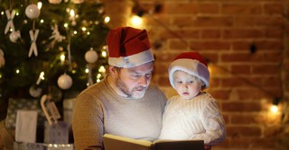 Dad and son, both wearing Santa hats, reading a book together