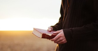 A man holding a Bible outside in a field