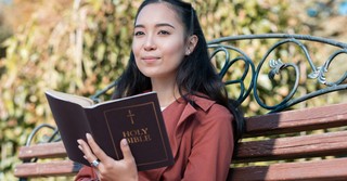 Woman reading the Bible on a park bench