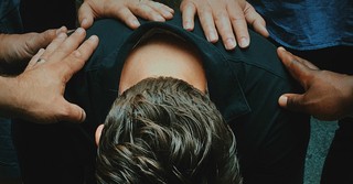 Man sitting with head bent, others laying hands on him in prayer