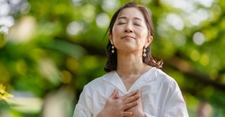 Peaceful older woman outside with her hands over her heart