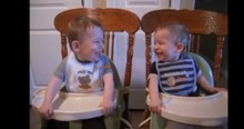 Twin Baby Boys Laugh At Each Other In Their Highchairs During Dinnertime
