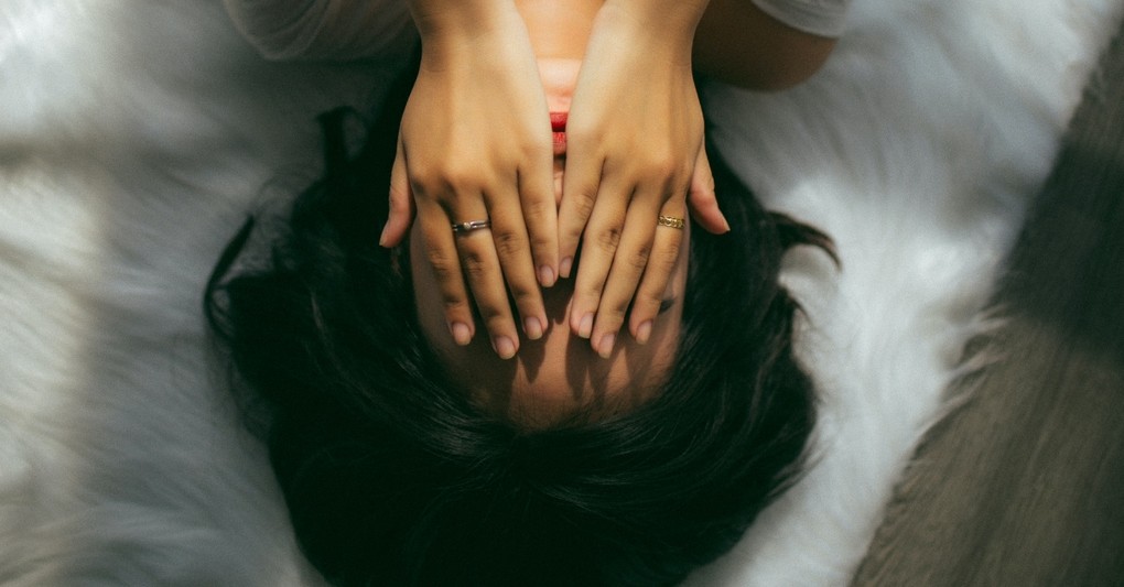young woman lying on her bed with hands over face looking afraid and stressed and sad