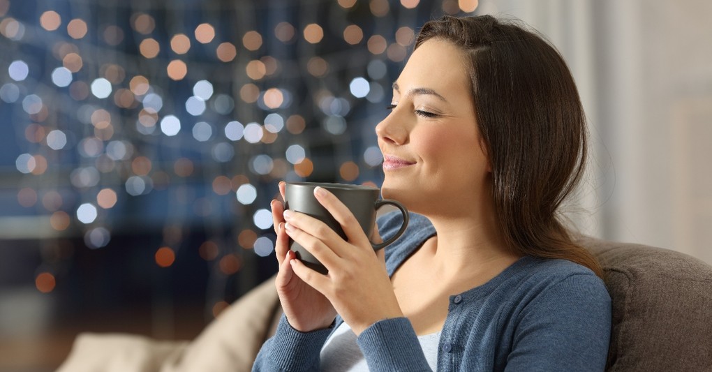 woman smiling sitting on couch with mug looking relaxed and peaceful