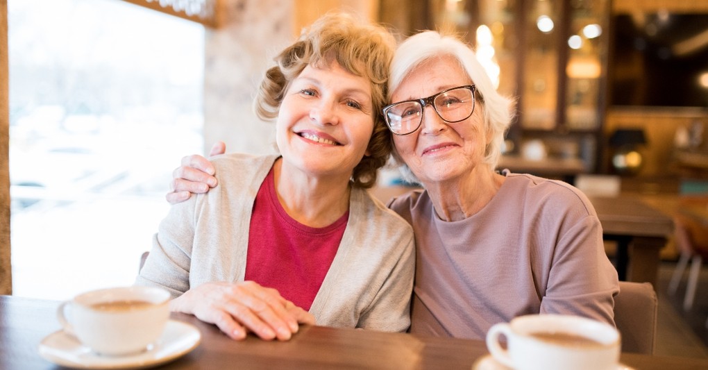 two white senior women smiling and side hugging at cafe enjoying friendship, beauty and fashion mistakes mature women make
