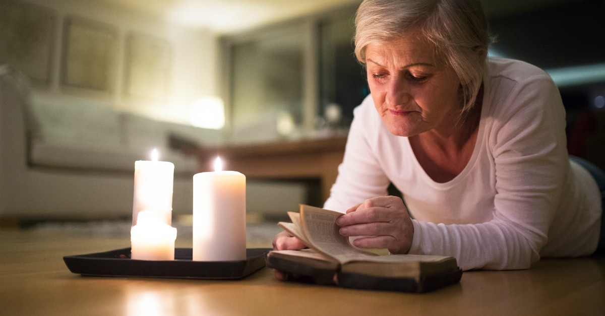 senior woman relaxing on floor with candles reading Bible