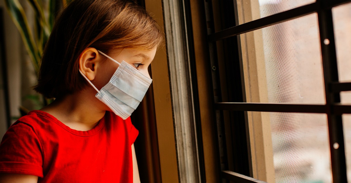 sick child with face mask on looking out window