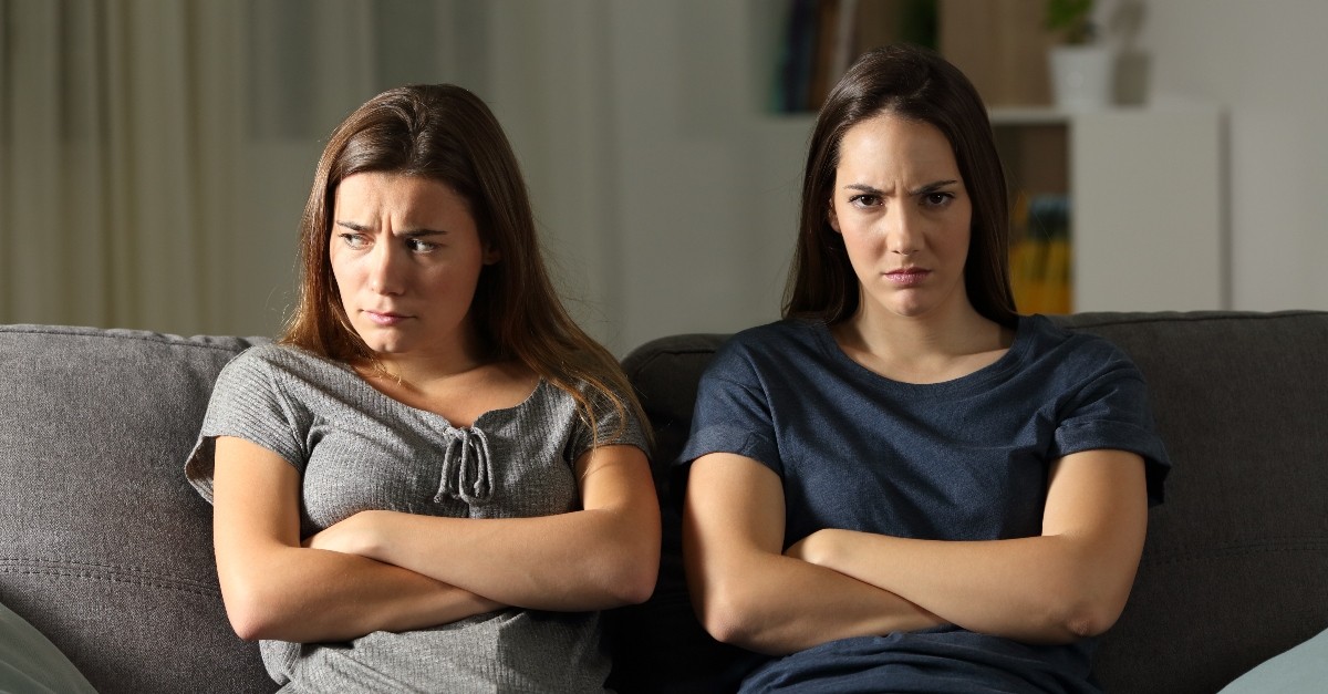 two women sitting on couch with crossed arms looking upset and angry, people don't listen to each other