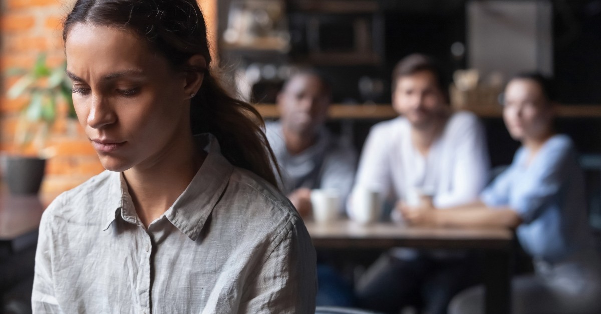 woman looking sad standing alone far from a group