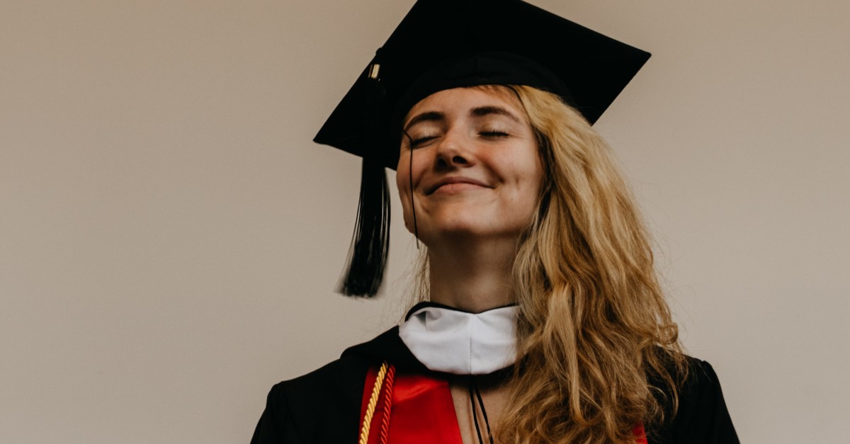young woman in graduation cap and gown eyes closed smiling