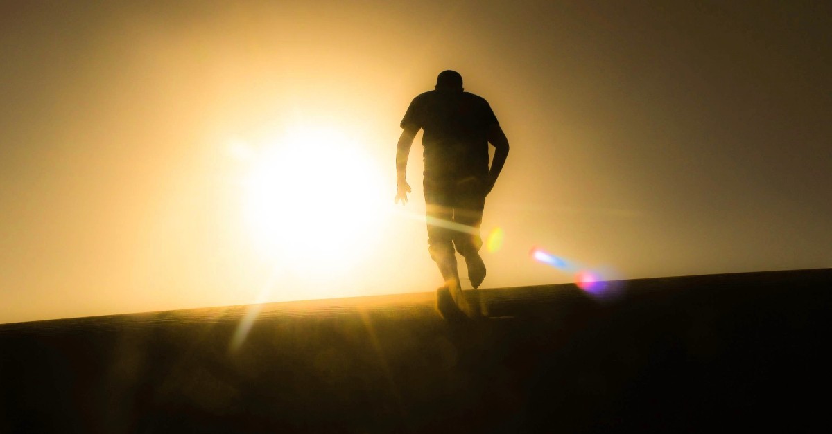 rear view of silhouette man running up hill toward sunset