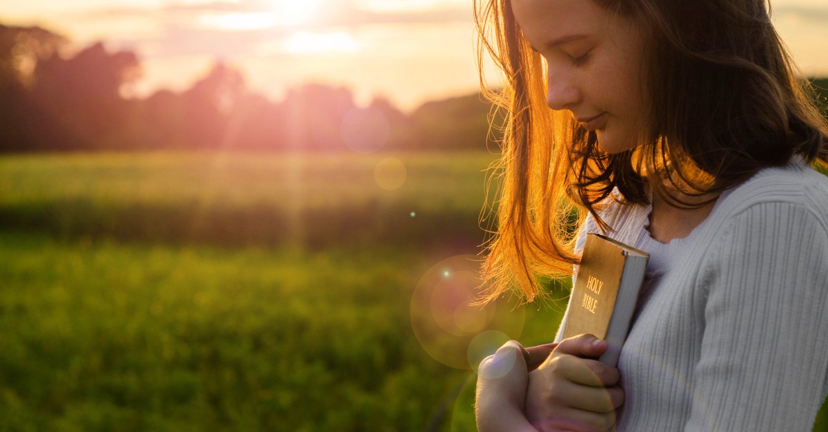 teen holding bible at sunset looking down peacefully
