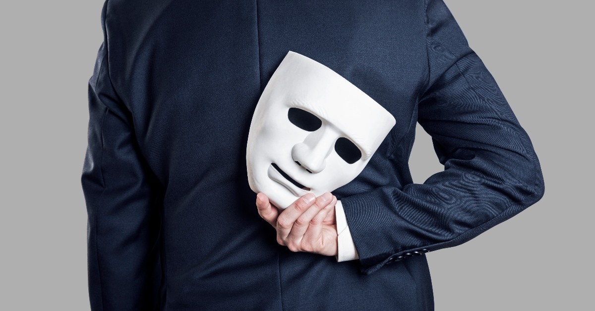 man in suit holding white mask behind his back