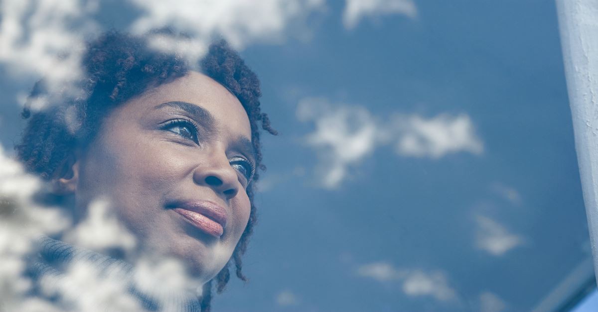 woman gazing through window reflecting clouds