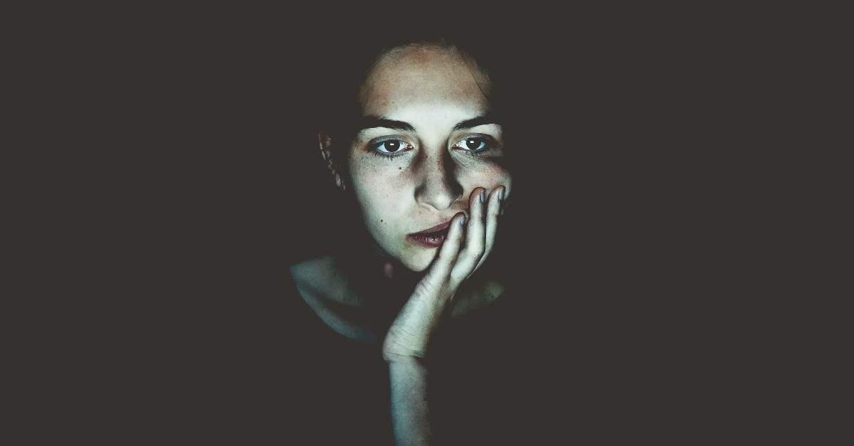 woman looking unsure or distressed in a dark space with electronic light on her face