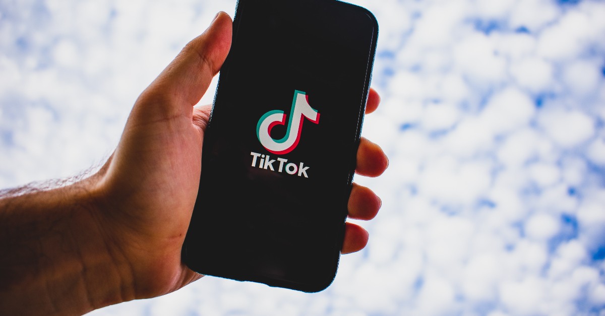 hand holding cell phone with TikTok logo up to blue cloudy sky