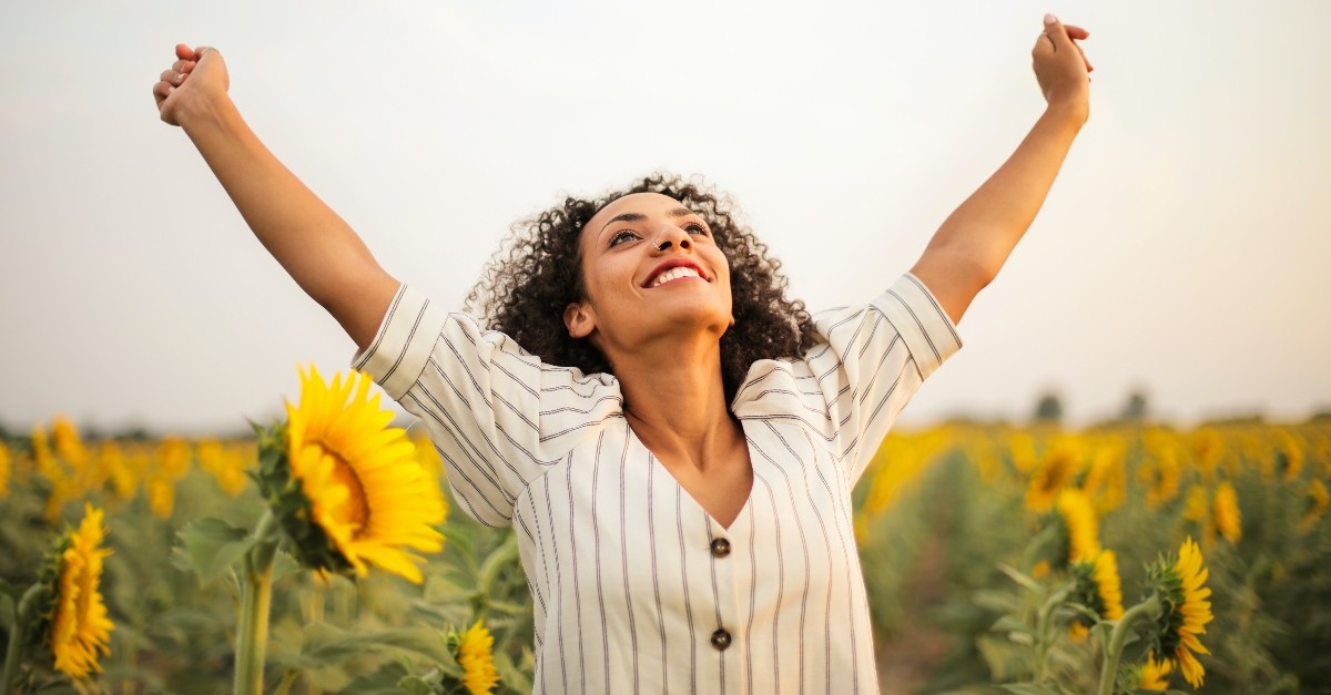 happy and joyful woman with arms in the air in a sunflower field, wonderful time to be alive