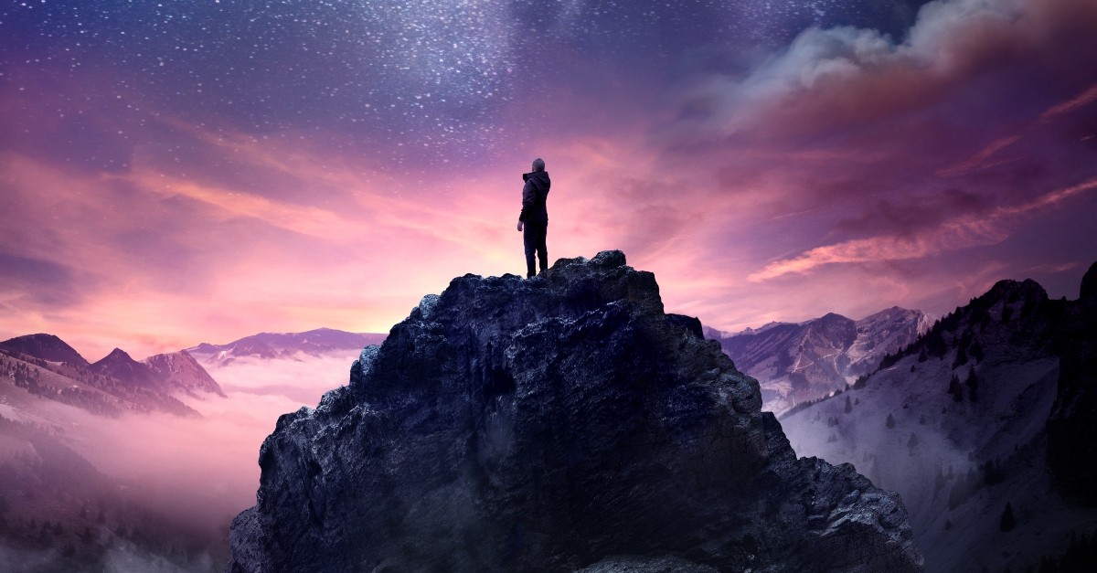 person standing on rocky outcrop looking at beautiful universe, God will never leave you