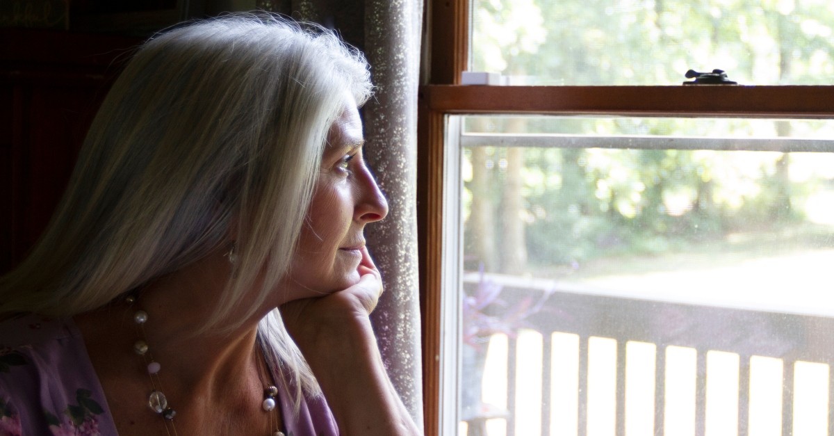 mature senior woman looking out window reflecting