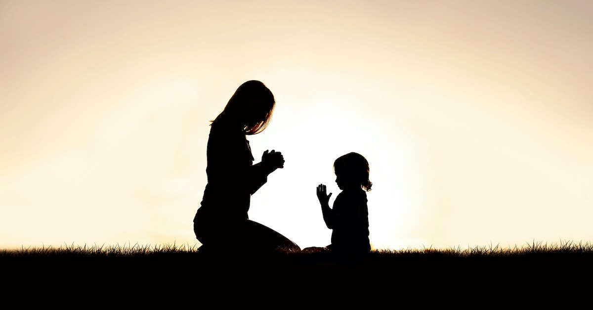 silhouette at sunset of mother and daughter praying outside, protection