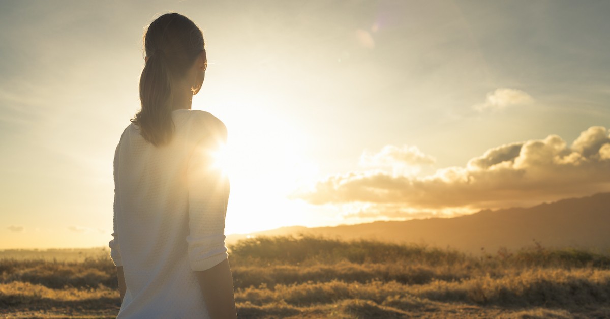 hopeful woman looking out toward sunrise over field