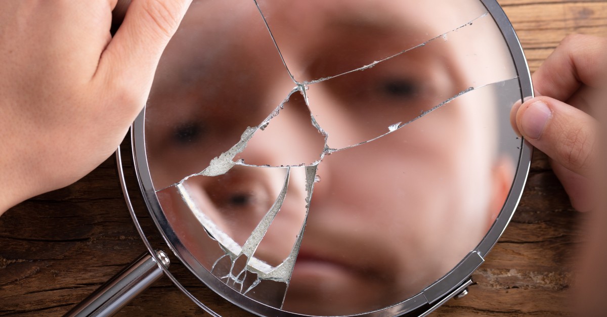 man looking into broken hand mirror