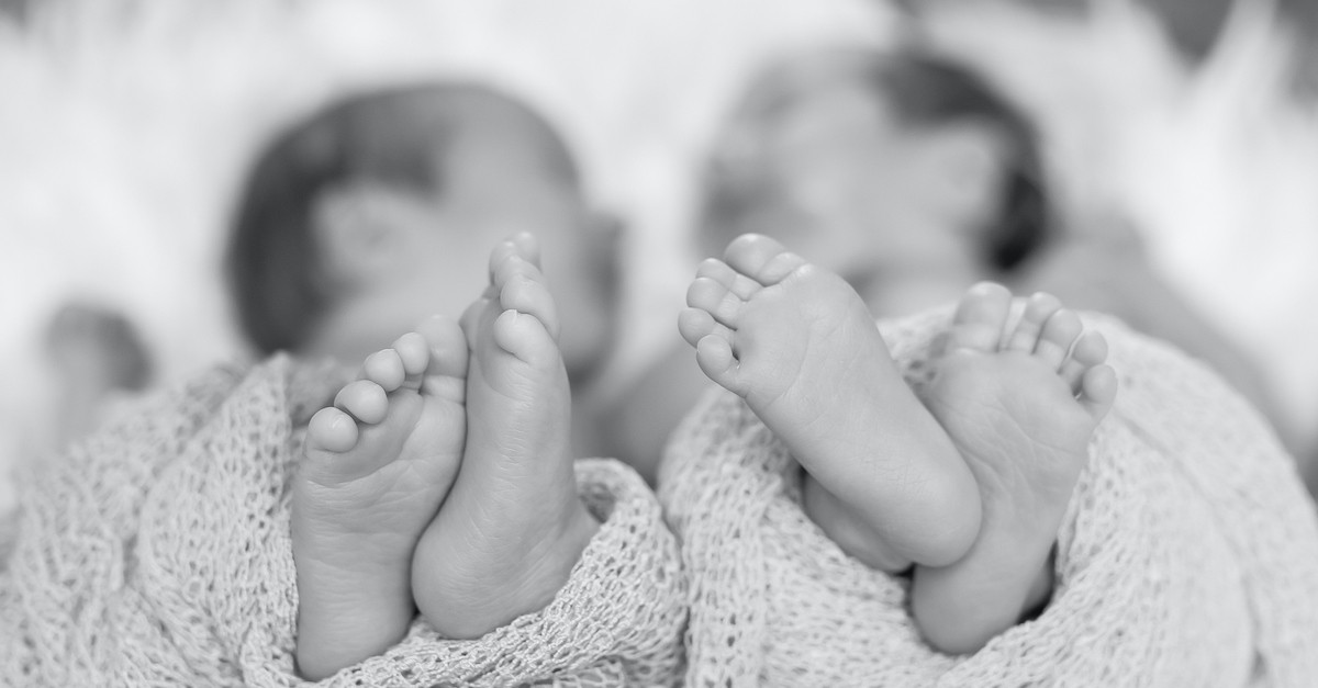 twin baby brothers next to each other with feet stick out in black and white photo