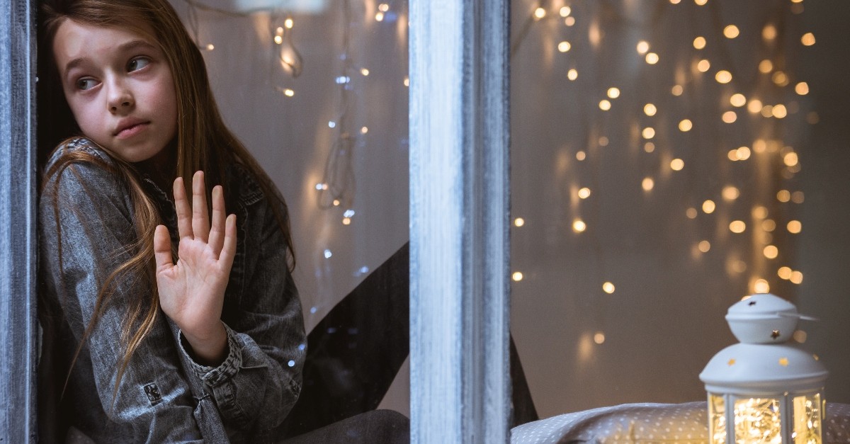 young girl looking sad in window at christmas, when christmas doesn't look very merry
