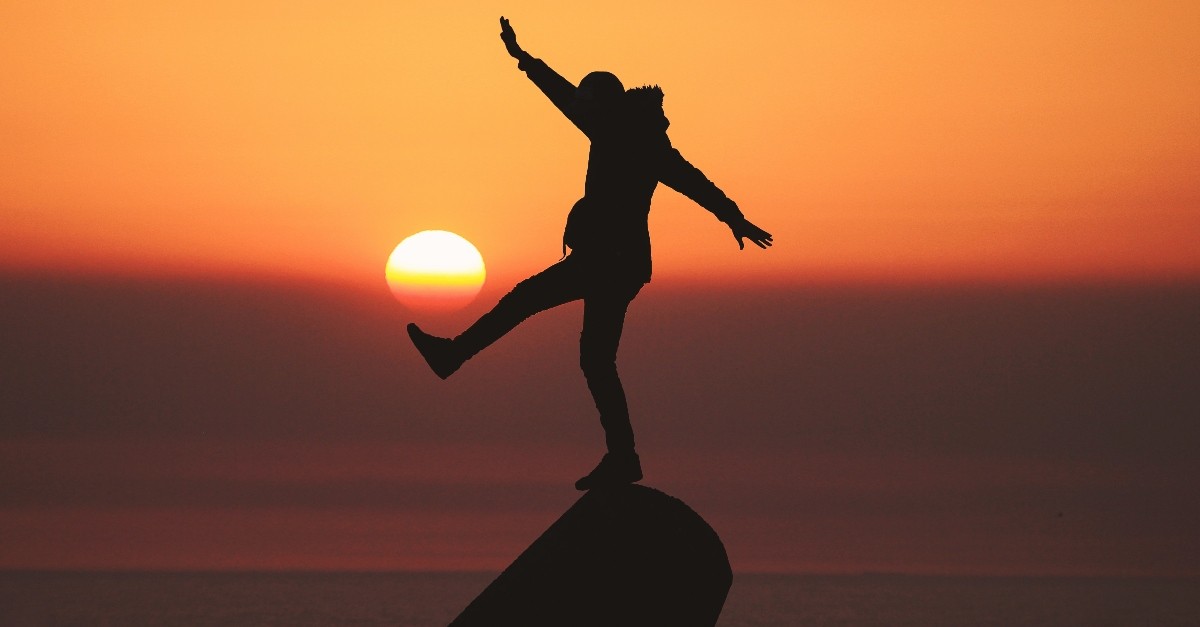 silhouette of person standing in front of setting sun looking excited