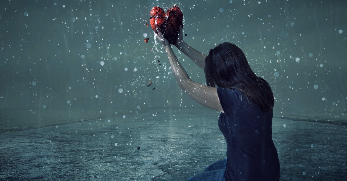 Woman holding a broken heart on her knees in the rain