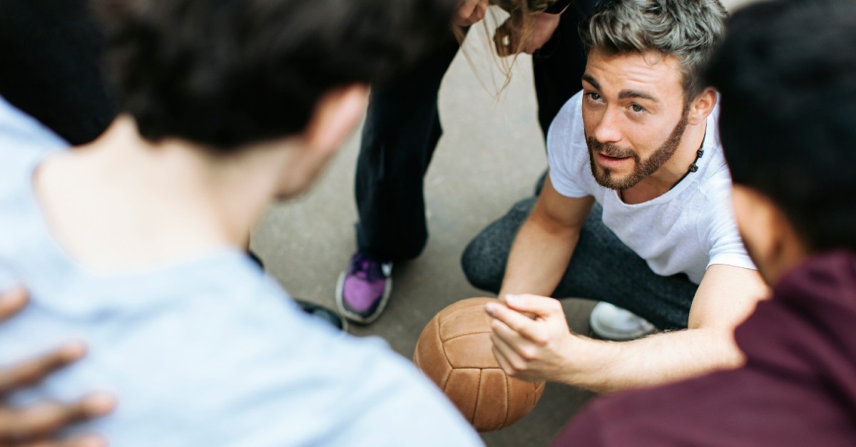 A young man volunteers his time to huddle a group of volleyball players