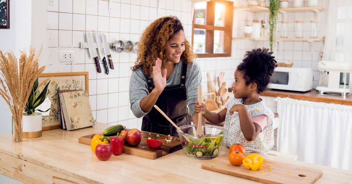 A mom high-fives her daughter as they prepare a healthy dinner