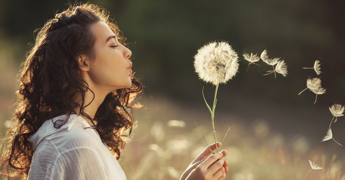 young woman blowing dandelion in field
