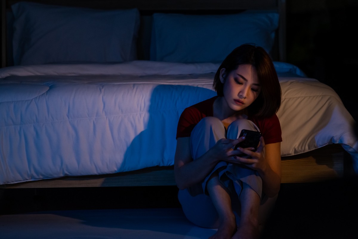young woman in room by herself in dark looking at phone