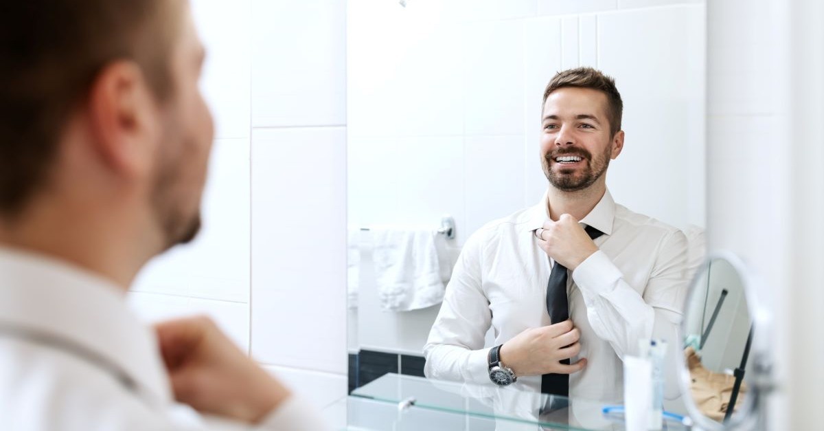 man looking in mirror fixing tie dressed up smiling bathroom getting ready