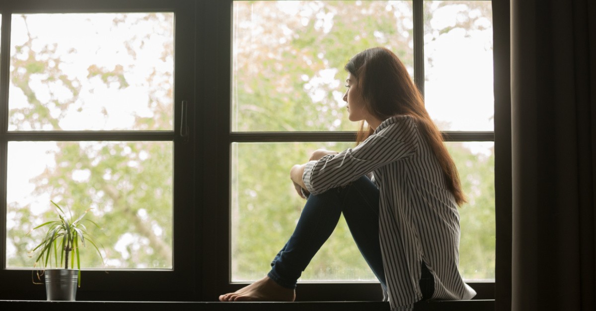 A sad millennial sitting on a window sill