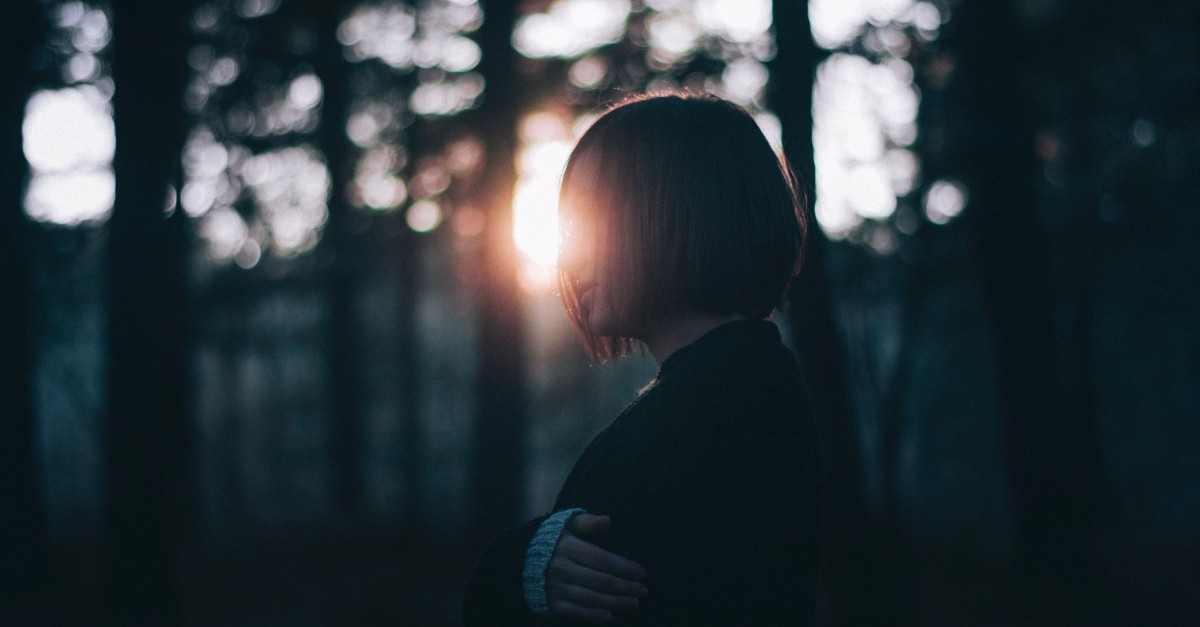 grieving woman walking through the gloomy woods, sunlight faintly shining in the background 
