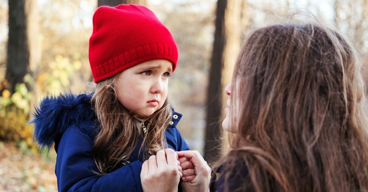 child in red cap holding mom's hands looking scared