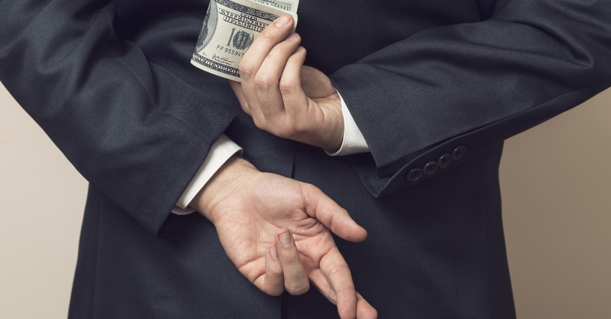 man with fingers crossed behind back holding stack of money to signify greed or deceit