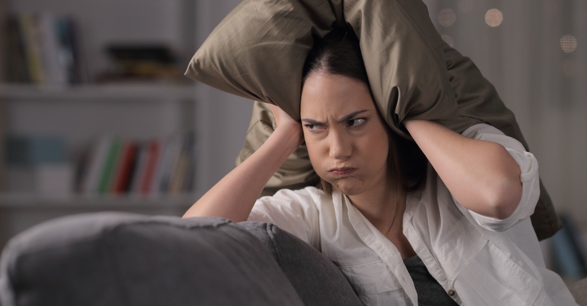 woman with a pillow over her head looking angry and frustrated