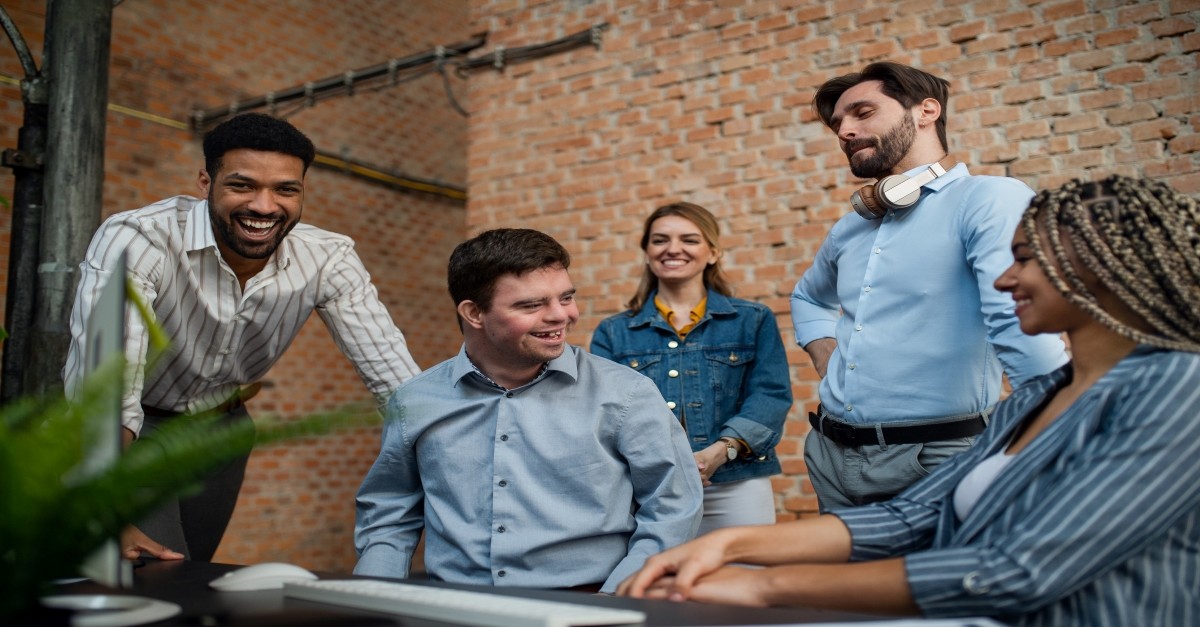 Happy down syndrome man with business colleagues in office, overcome evil with good