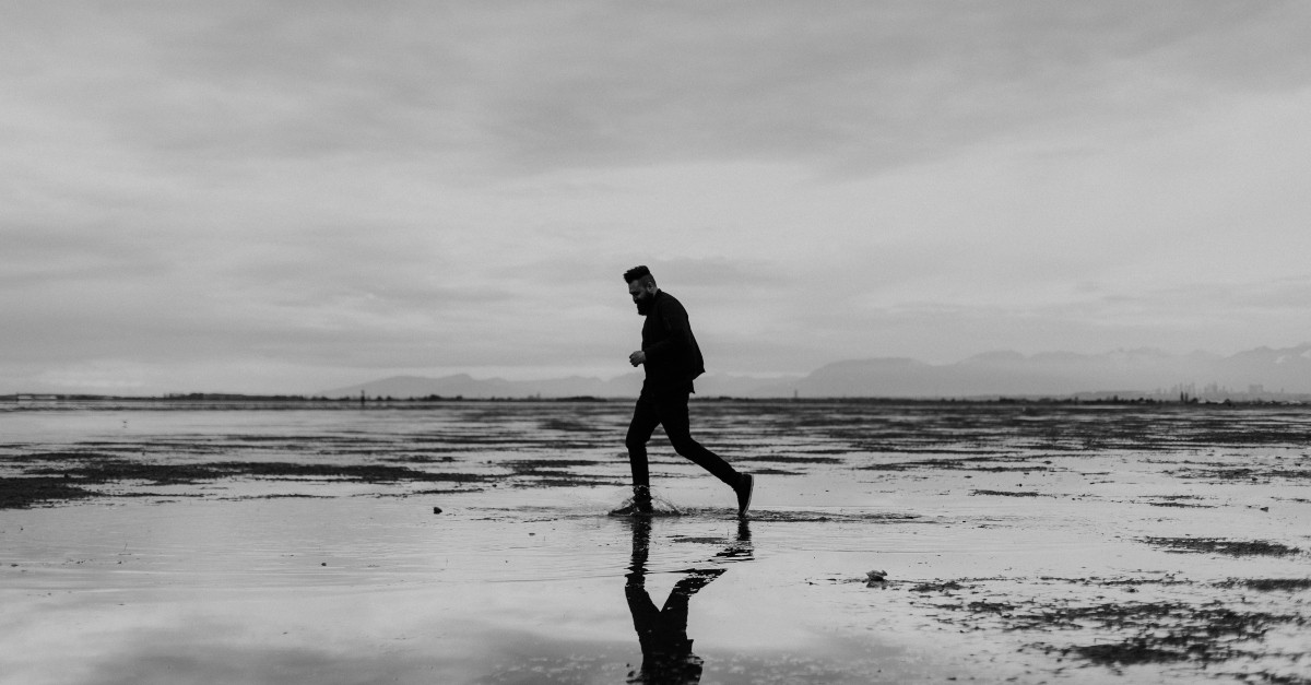 Black and white photo of a sad man walking along the water