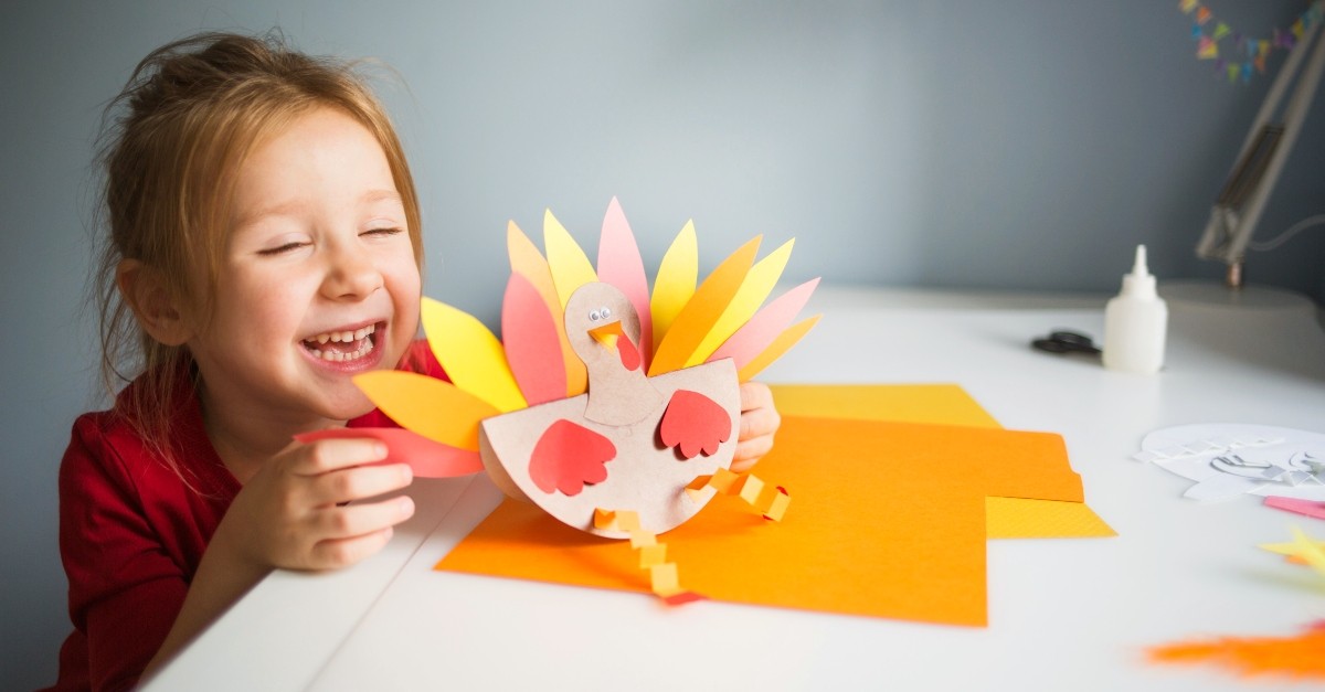Child making a paper turkey to illustrate thanksgiving games for younger kids