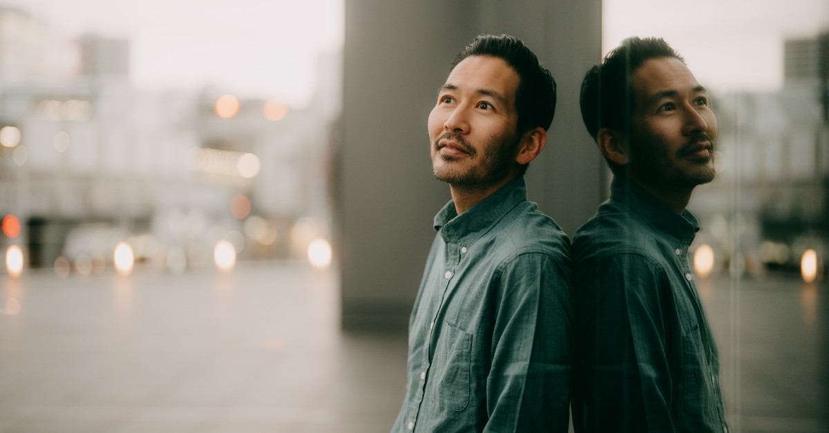 Asian man standing outside in a city, looking up, hopeful